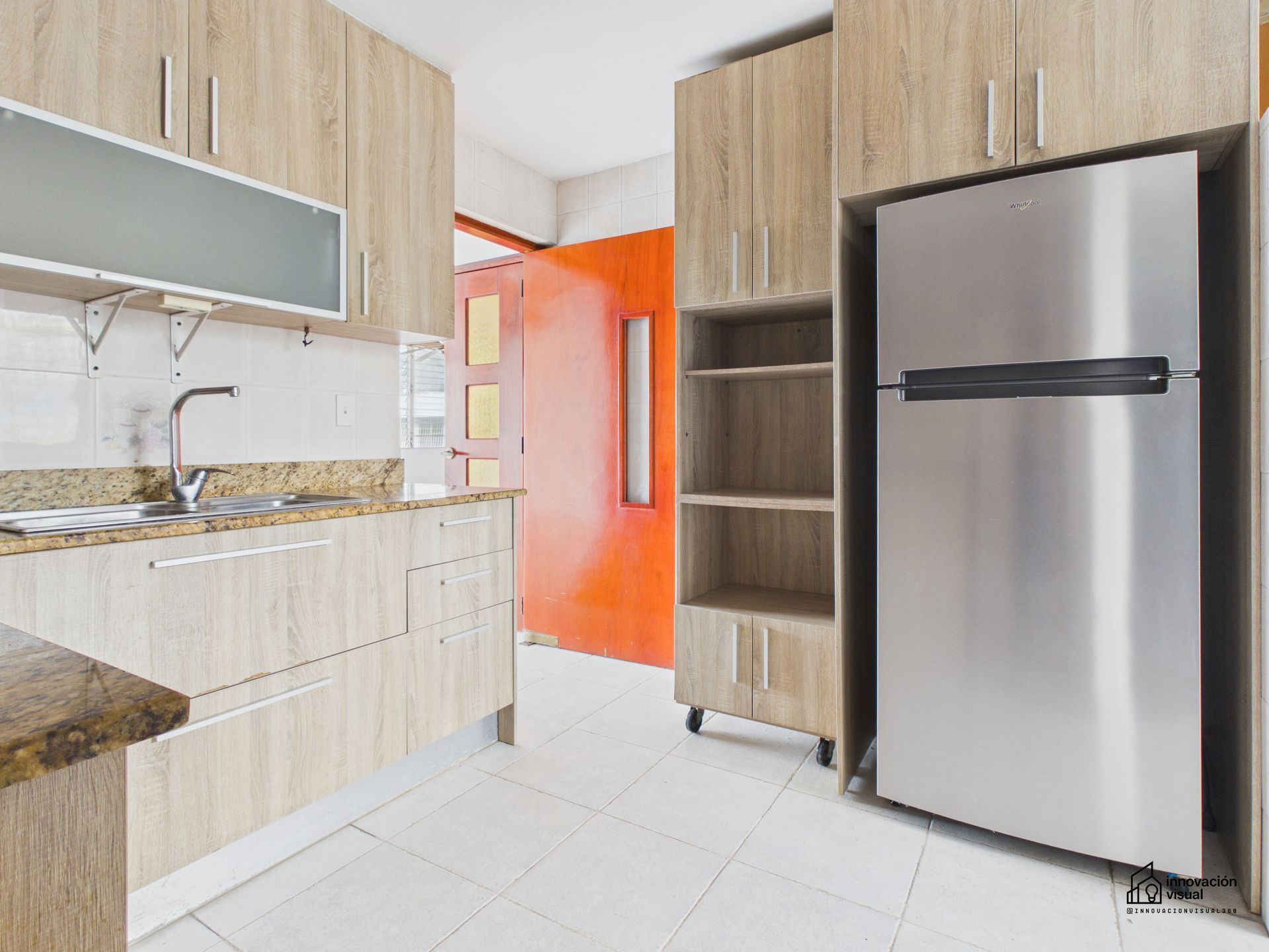 Cocina con gabinetes de madera clara, refrigerador de acero inoxidable y puerta naranja.