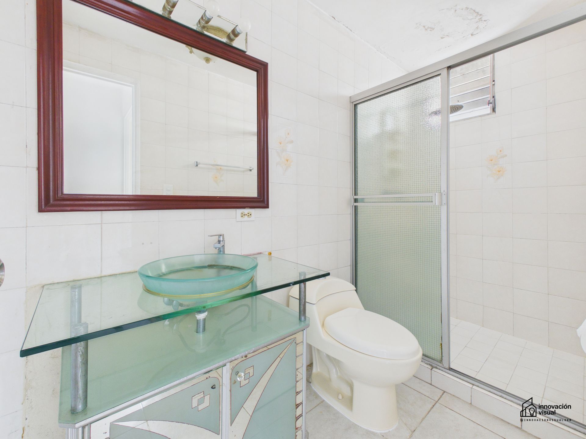 Baño con tocador con encimera de vidrio, lavabo de vidrio azul y ducha cerrada.