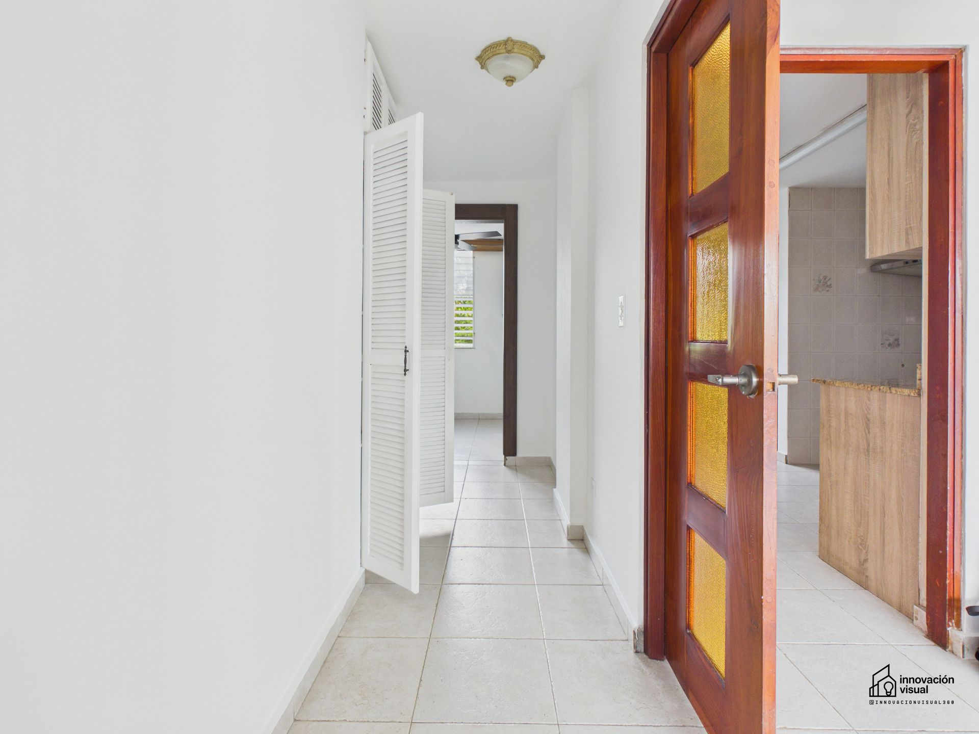 Pasillo con paredes blancas, suelo de baldosas y puertas abiertas que conducen a las habitaciones.