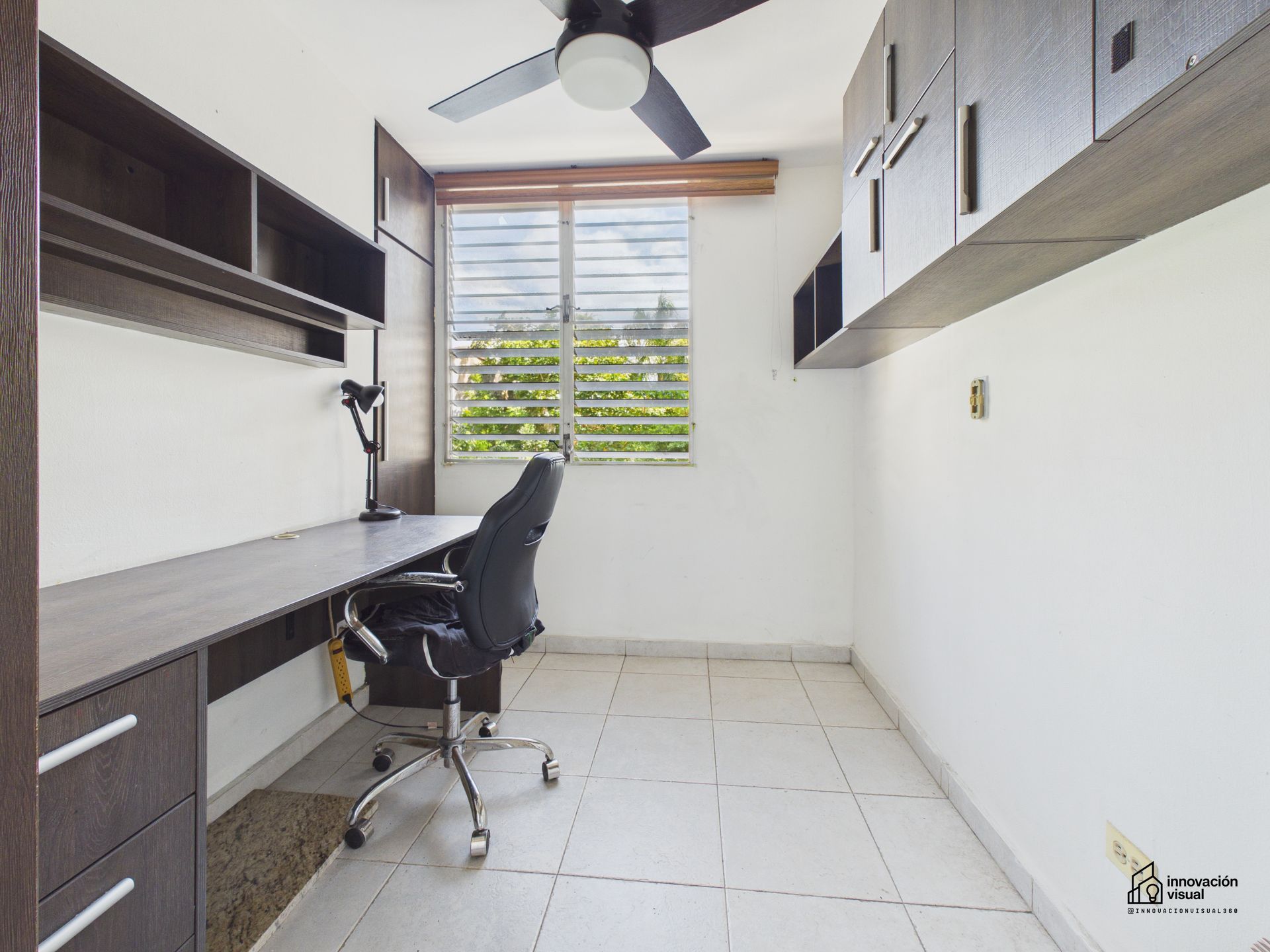 Oficina en casa con escritorio, silla, ventana y estantes empotrados.