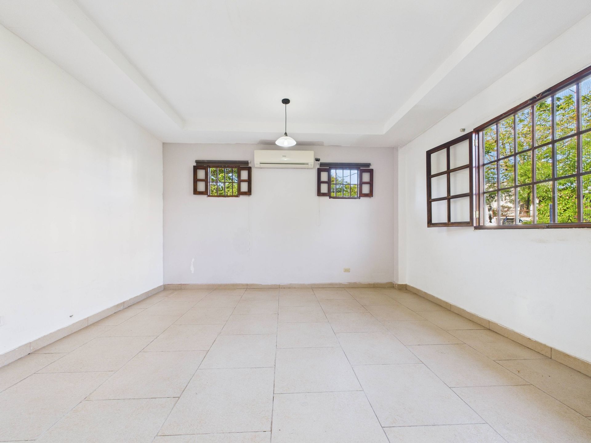 Habitación vacía con paredes blancas, suelo de baldosas y tres ventanas con vistas al exterior.