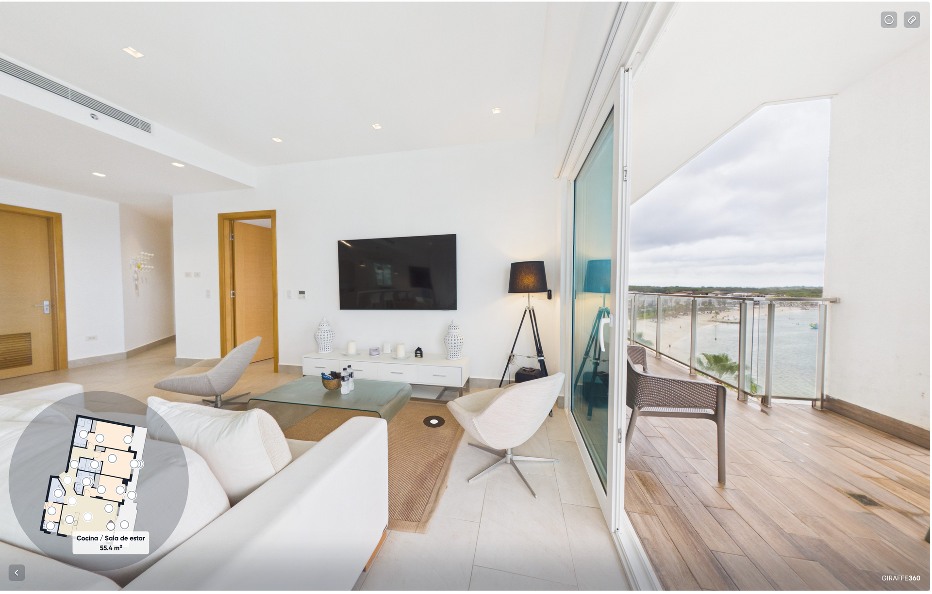 Bright modern living room with white sofa, wall TV, and open balcony overlooking the water