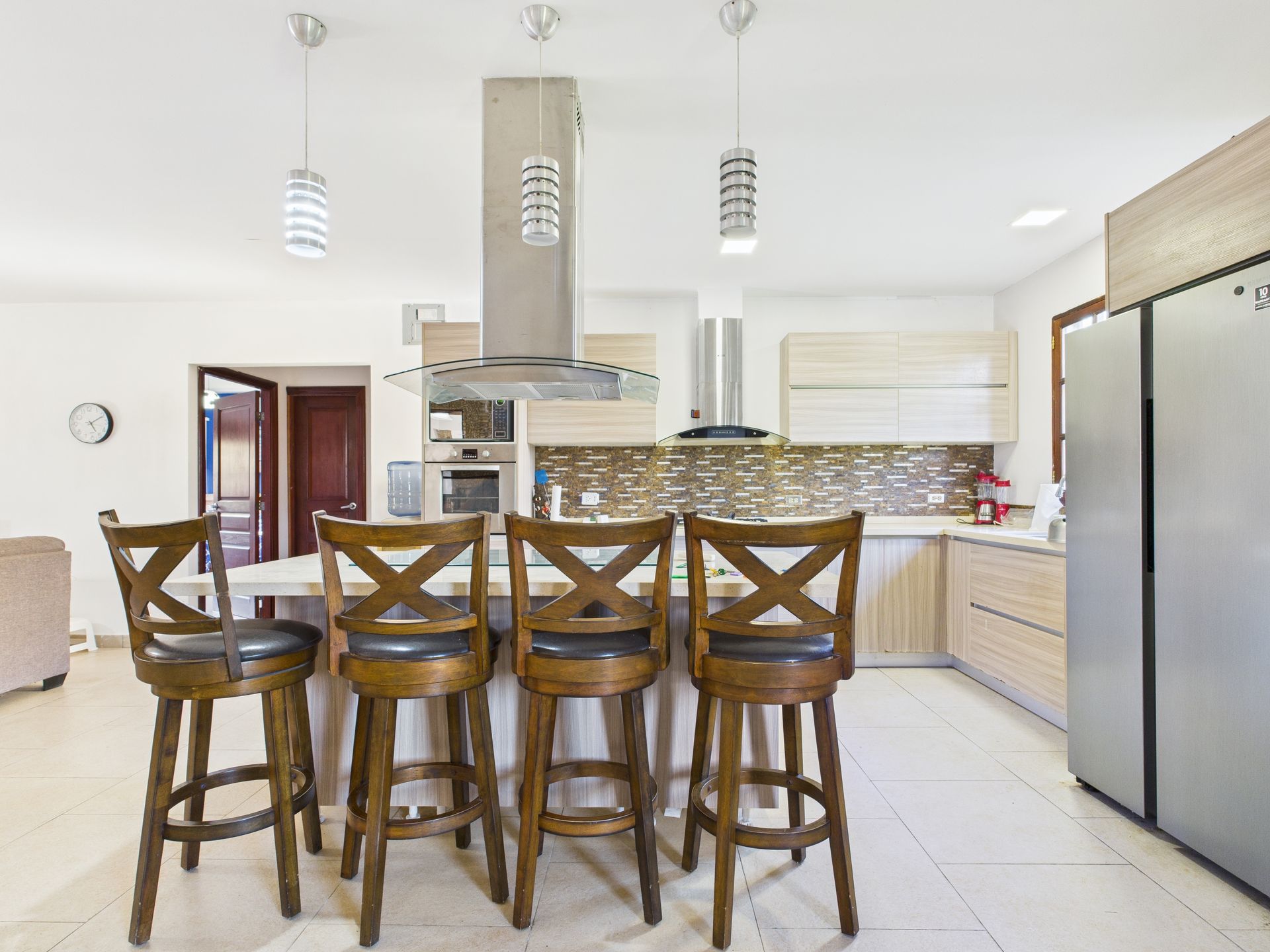 Cocina con isla, taburetes de madera, electrodomésticos de acero inoxidable y gabinetes de madera clara.