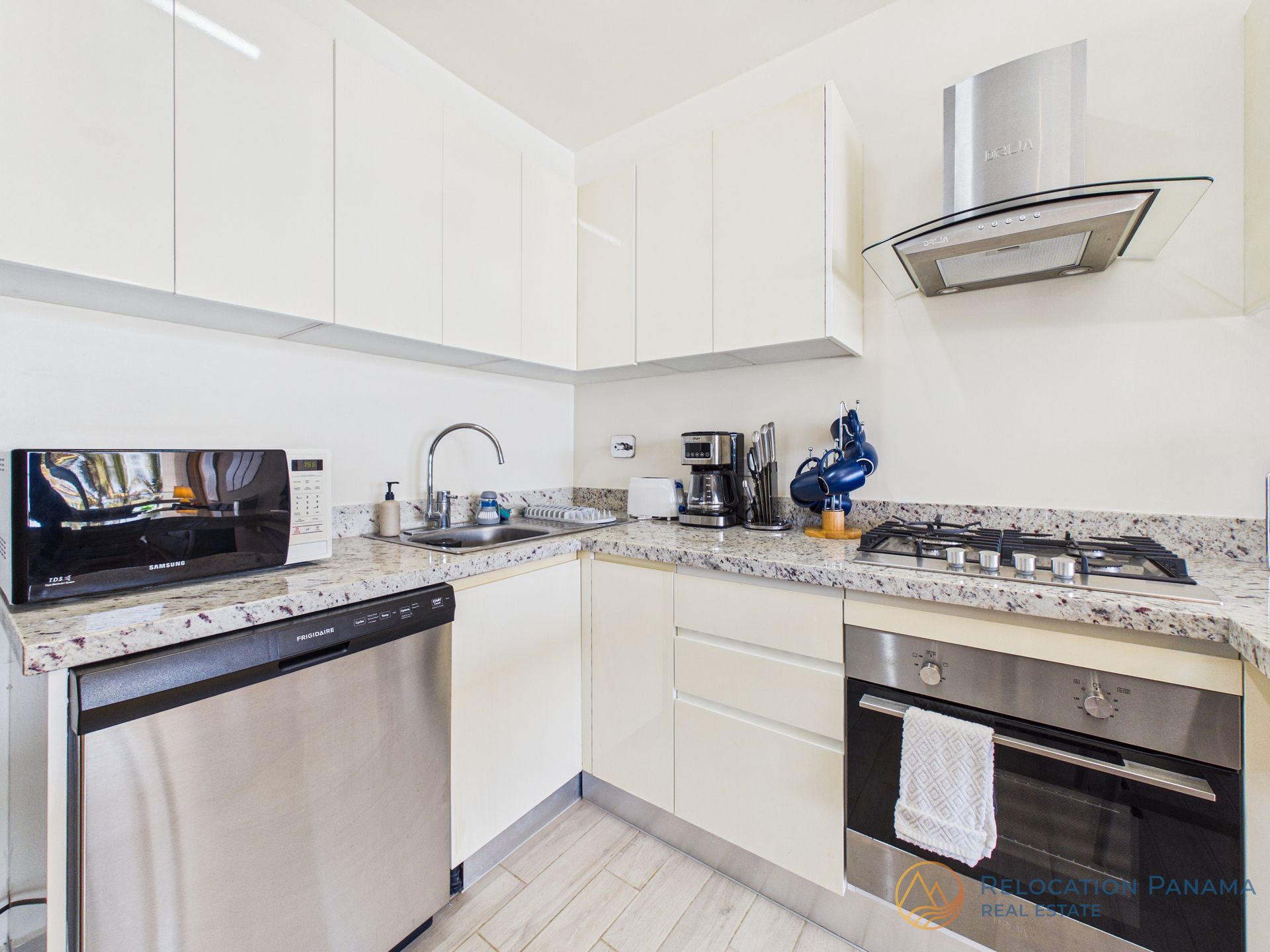 Cocina moderna y luminosa con armarios blancos, electrodomésticos de acero inoxidable y encimeras de granito.