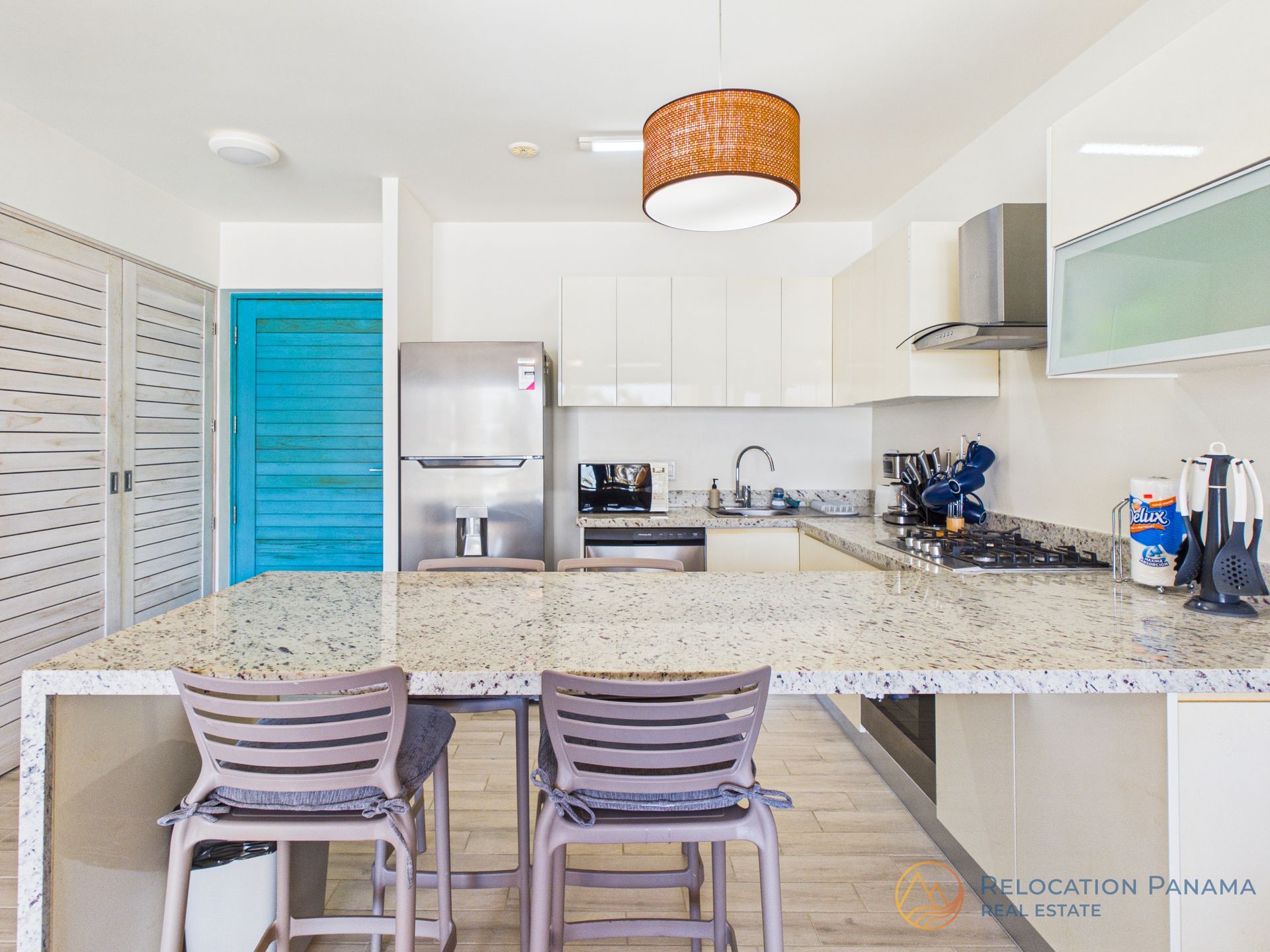 Cocina moderna con gabinetes blancos, isla de granito, refrigerador de acero inoxidable y puertas azules.