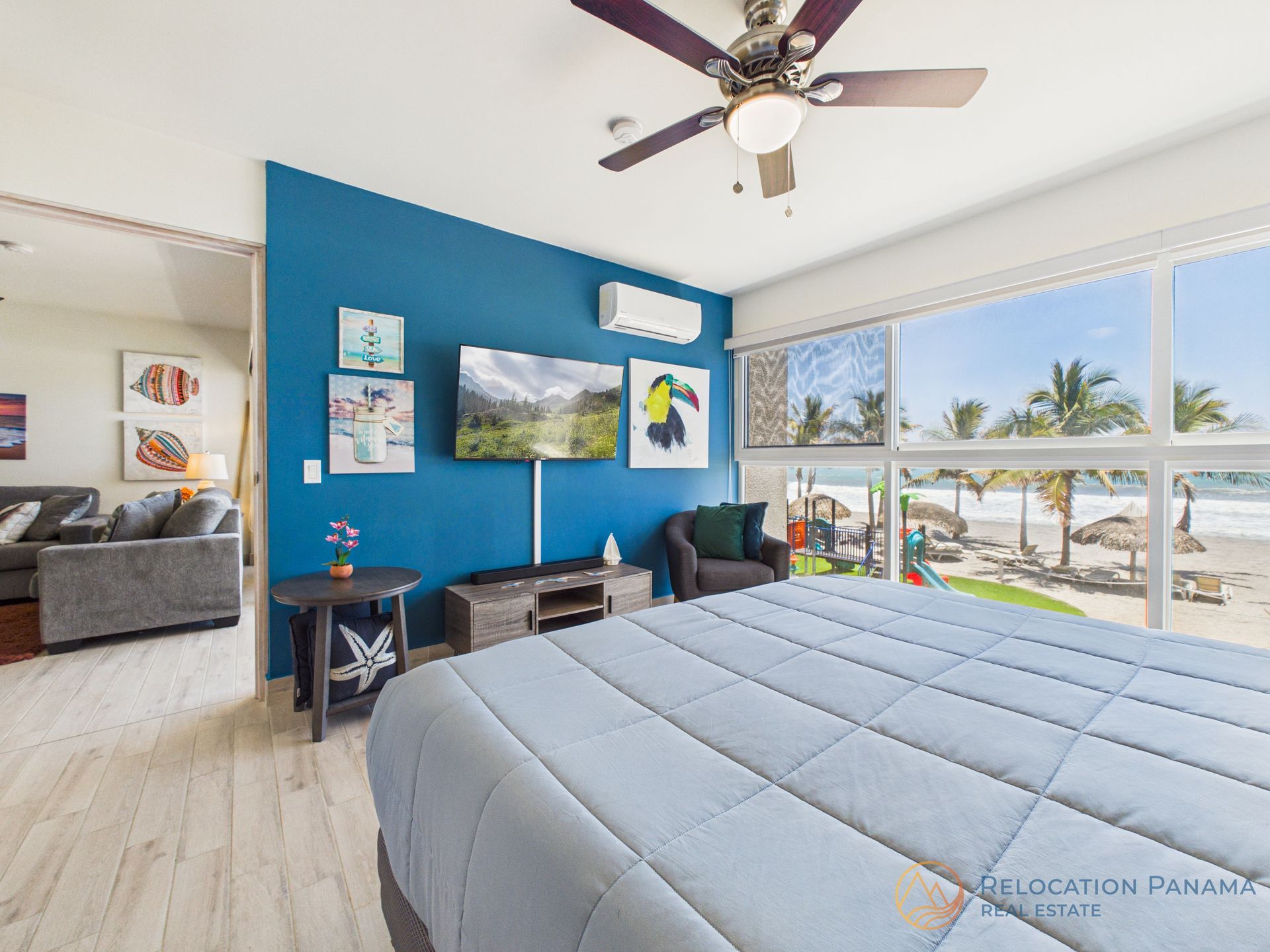 Habitación luminosa con una pared decorativa azul, cama king size, televisor, ventilador de techo y grandes ventanales con vistas a una piscina.