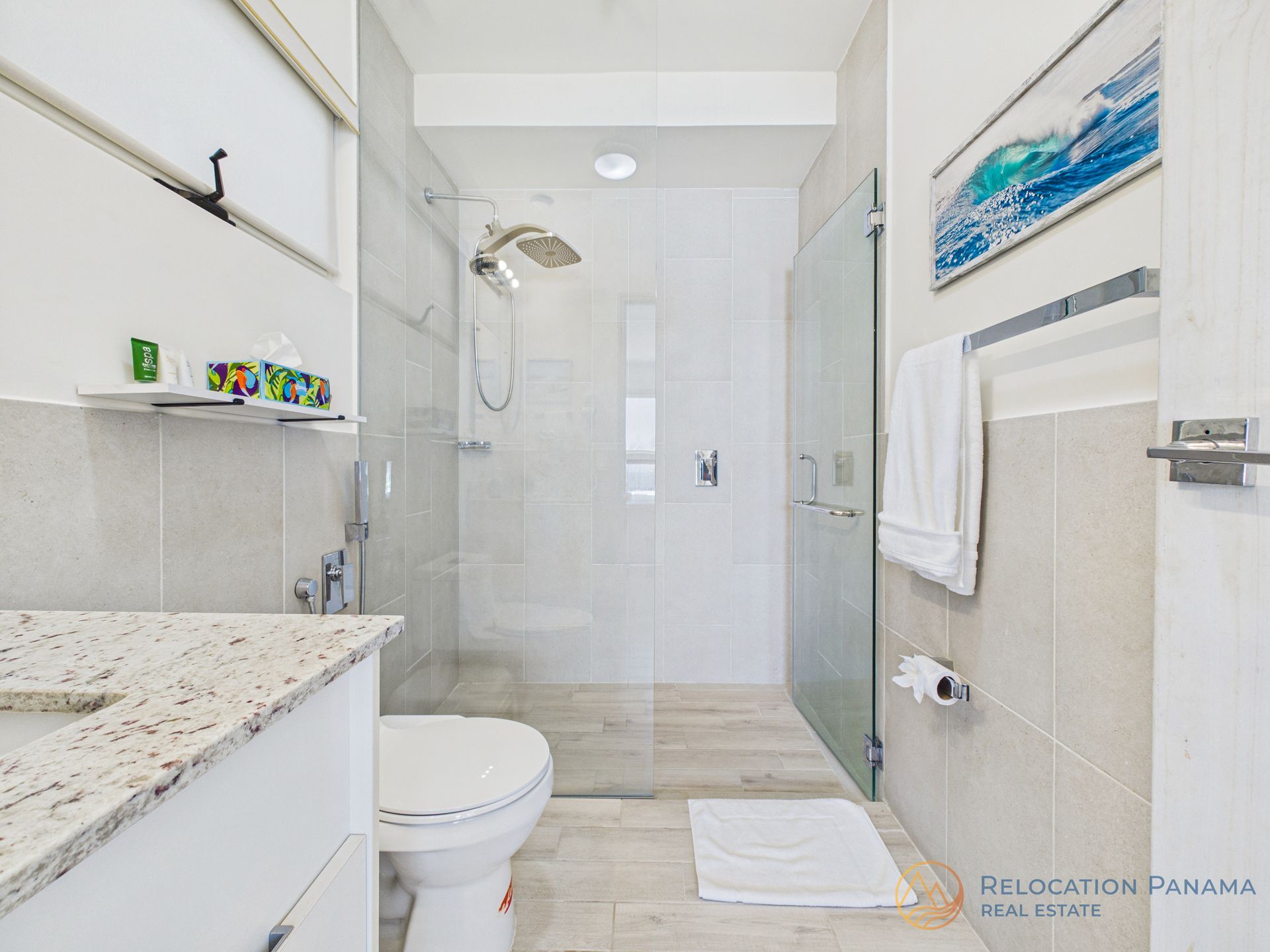 Baño moderno blanco con ducha de cristal, inodoro, lavabo y toallero.