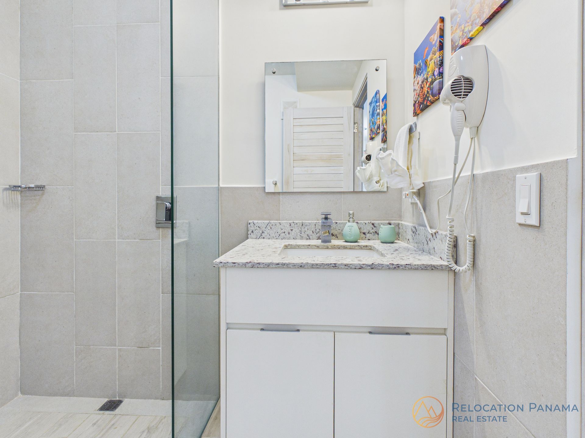 Tocador de baño luminoso con espejo, encimera de granito y ducha alicatada a la izquierda.