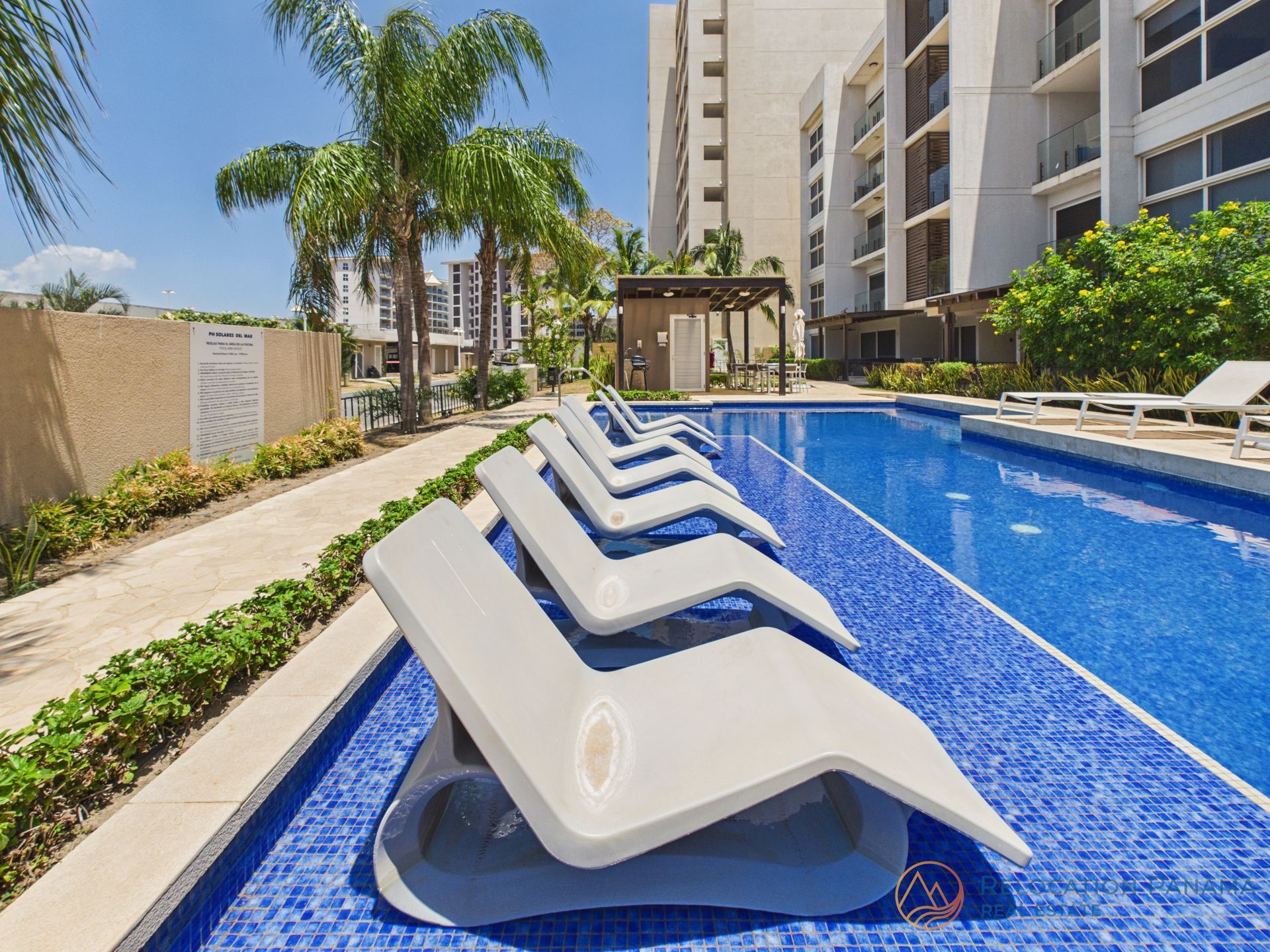 Tumbonas junto a una piscina azul en un moderno complejo de apartamentos.