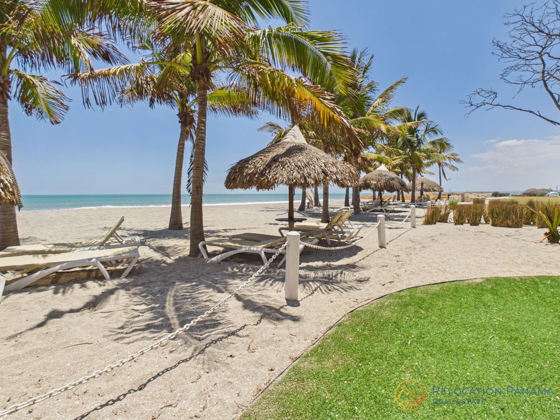 Playa tropical con palmeras, cabañas de paja y arena blanca junto a aguas turquesas.