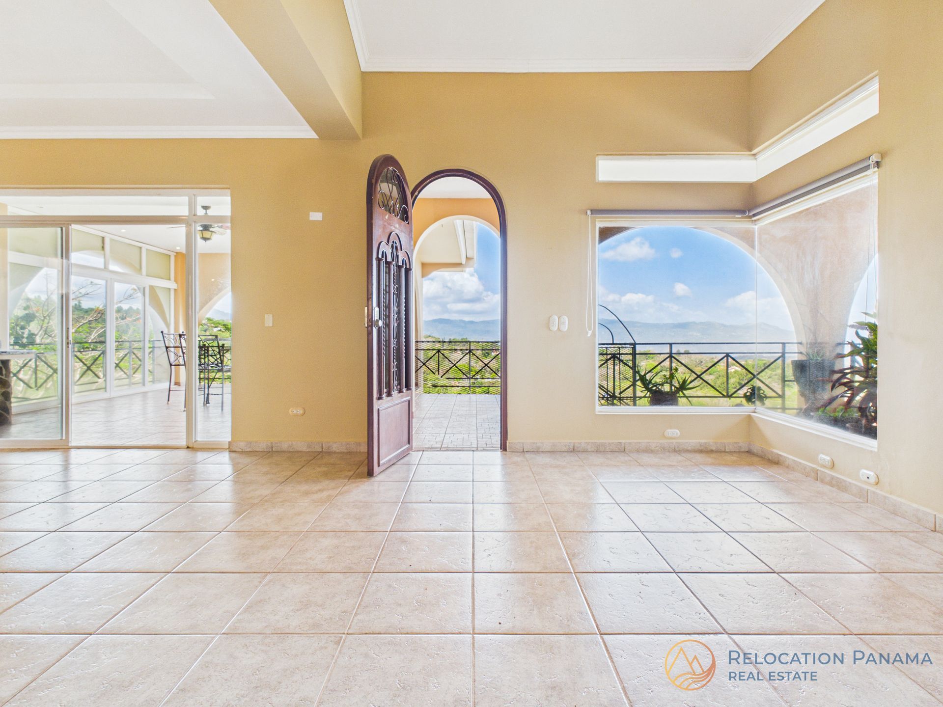 Habitación vacía con suelo de baldosas, puerta arqueada y grandes ventanales con vistas a un balcón y al océano.