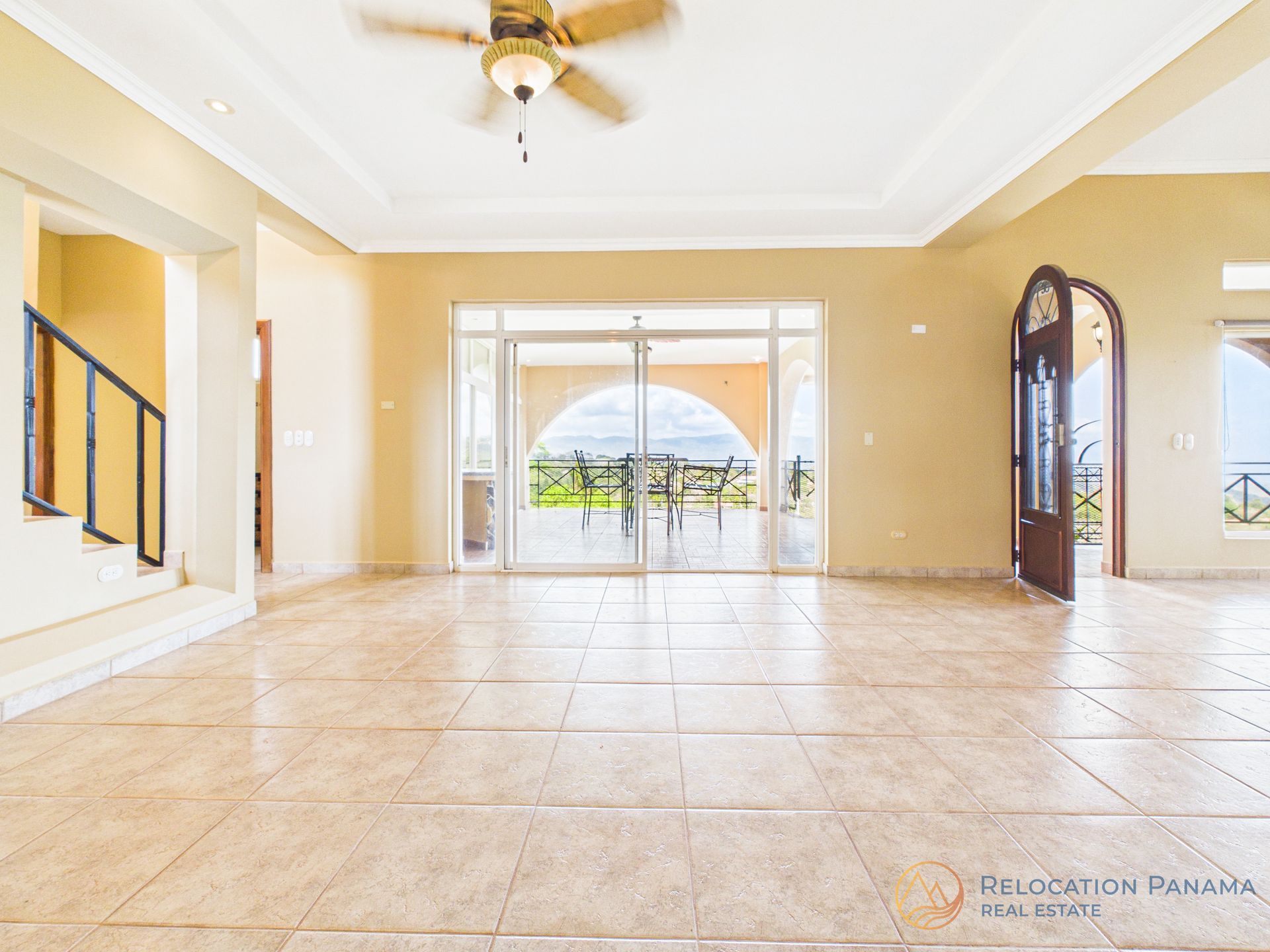 Sala de estar luminosa y vacía con suelo de baldosas, ventilador de techo y puertas arqueadas de cristal que dan a un patio.