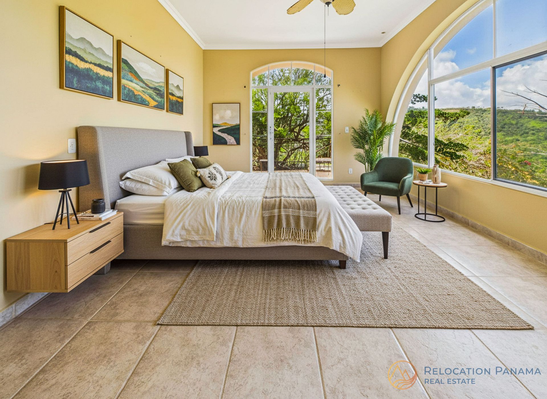 Habitación luminosa con ventanas arqueadas, decoración en tonos beige, una cama y un sillón con vistas a la vegetación.