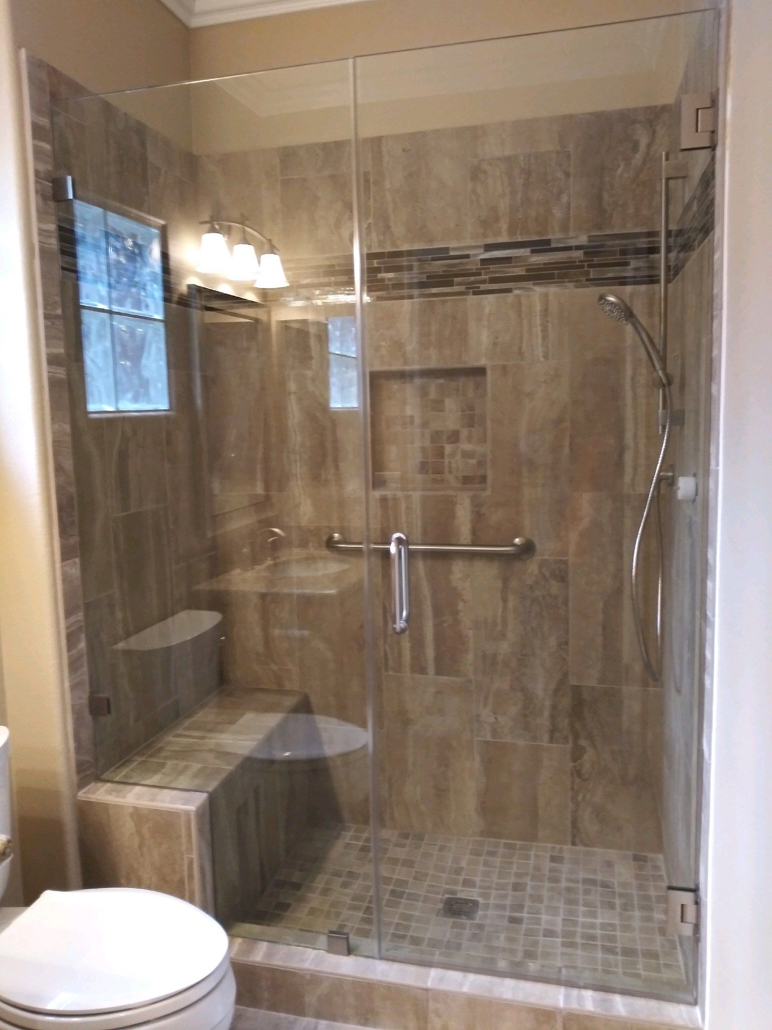 Accessible beige-tiled walk-in shower with grab bars, bench, and glass door in a bathroom