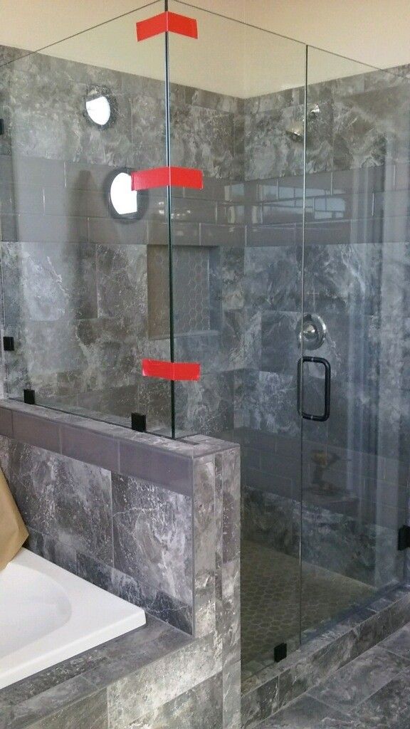 Glass shower enclosure with gray tile walls and a frosted panel beside a sink counter
