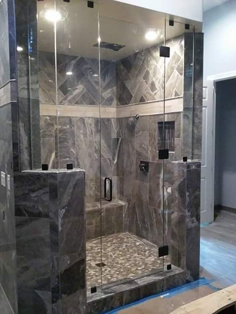 Glass-enclosed marble shower with gray tile walls, recessed shelves, and chrome fixtures