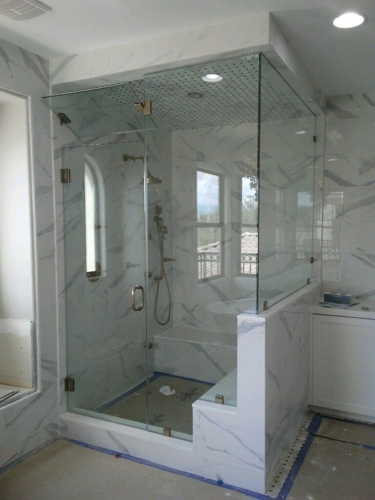 Glass walk-in shower with marble walls and a built-in bench in a bright bathroom