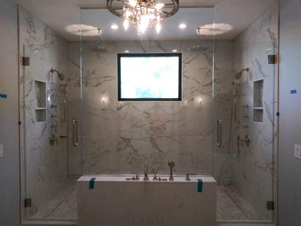 Modern bathroom with glass shower enclosure, marble walls, vanity, and chandelier-lit ceiling