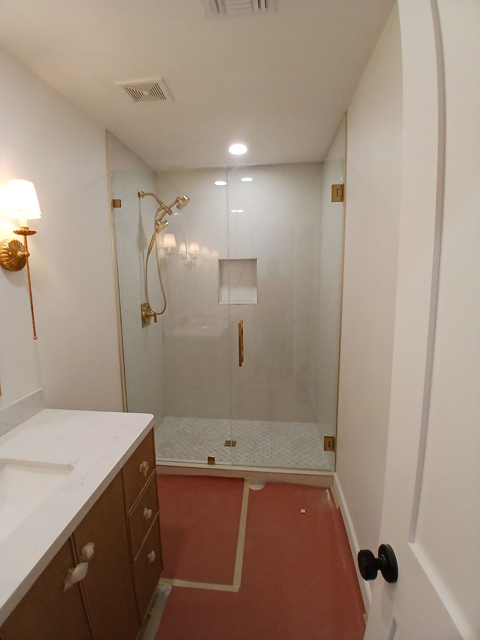 Narrow bathroom with shower, vanity cabinet, glass door, and partially finished floor tiles.