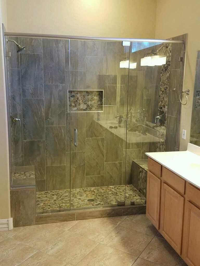 Glass shower enclosure with stone tile surround in a bathroom, next to a vanity and countertop.
