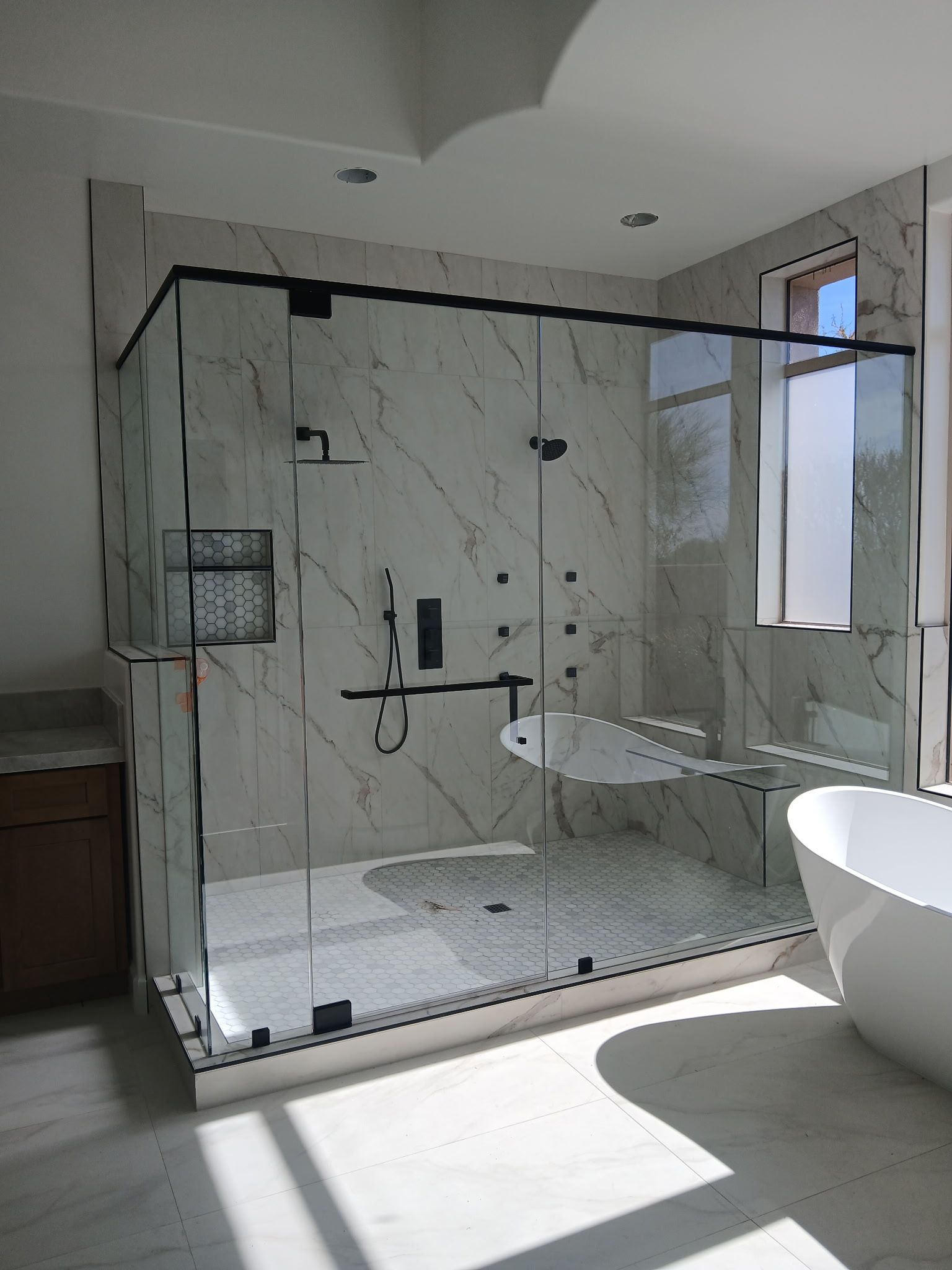 Modern marble-tiled bathroom with glass shower, vanity, and sunlight on the floor