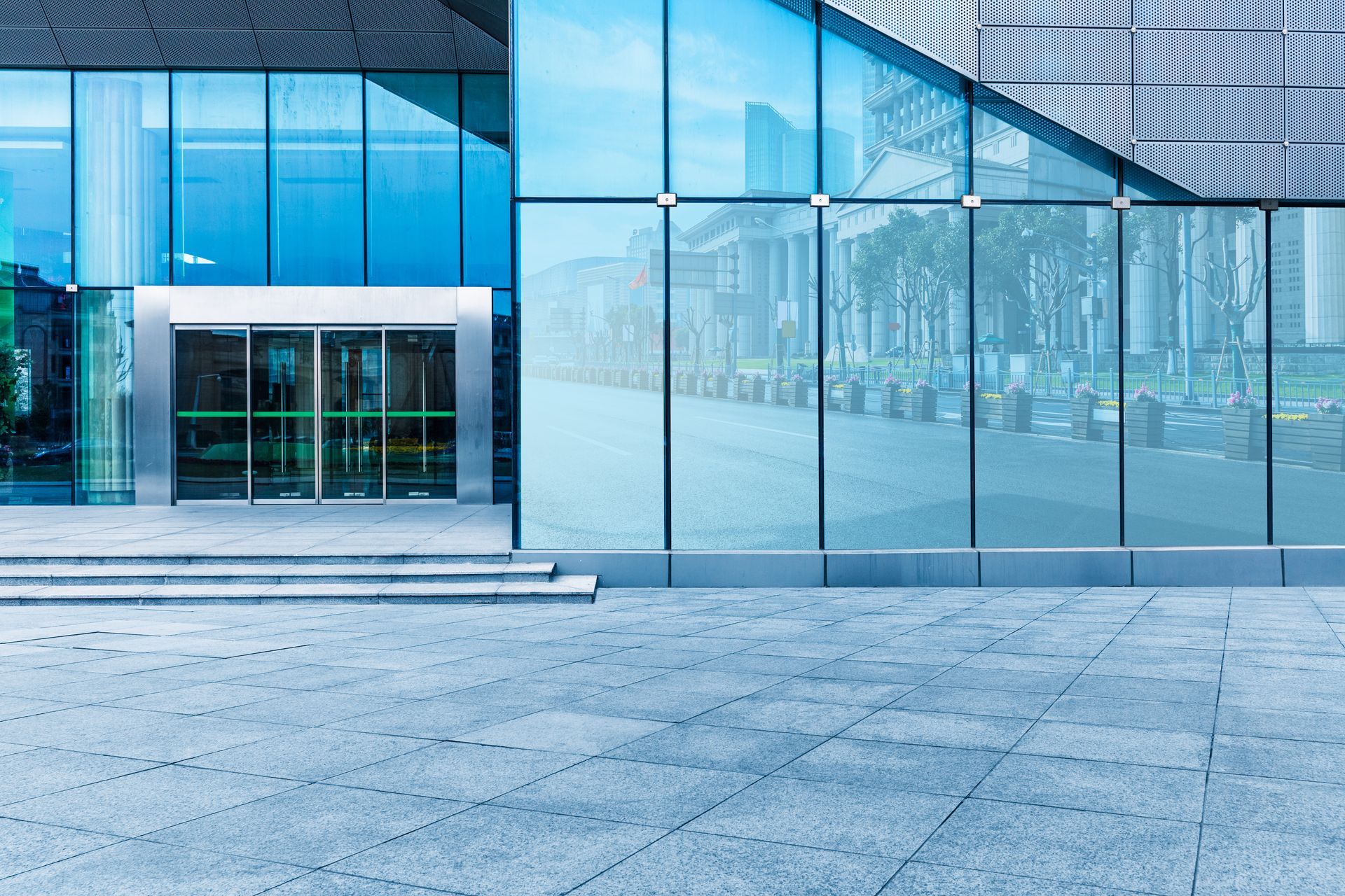 Modern glass office building entrance with blue-tinted windows and empty stone plaza