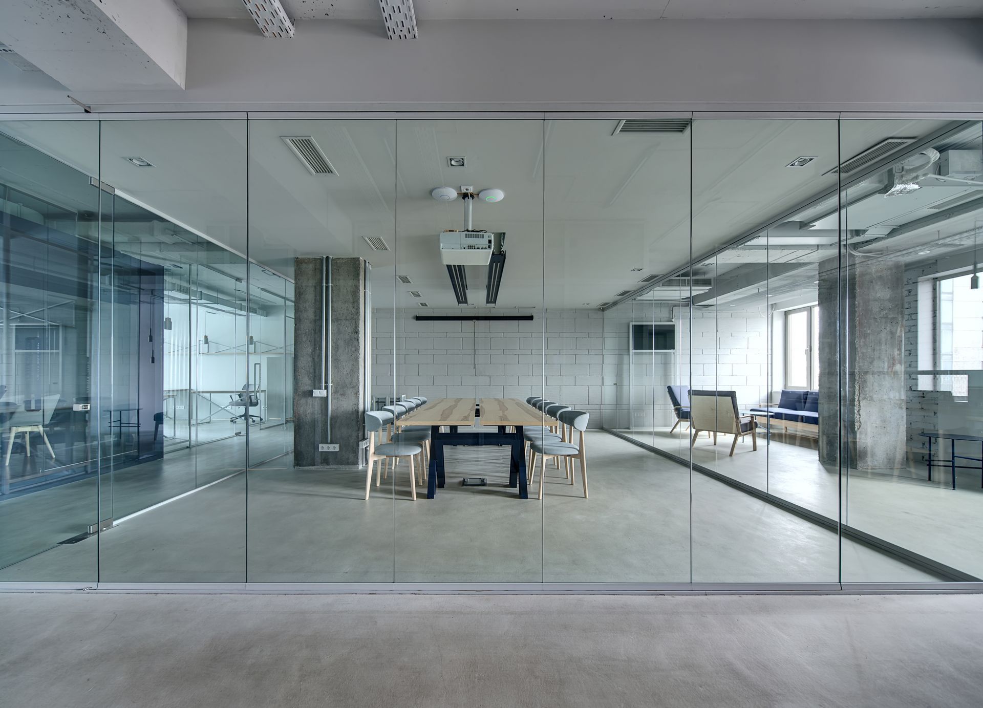 Modern glass-walled conference room with a long table and chairs in a bright office.