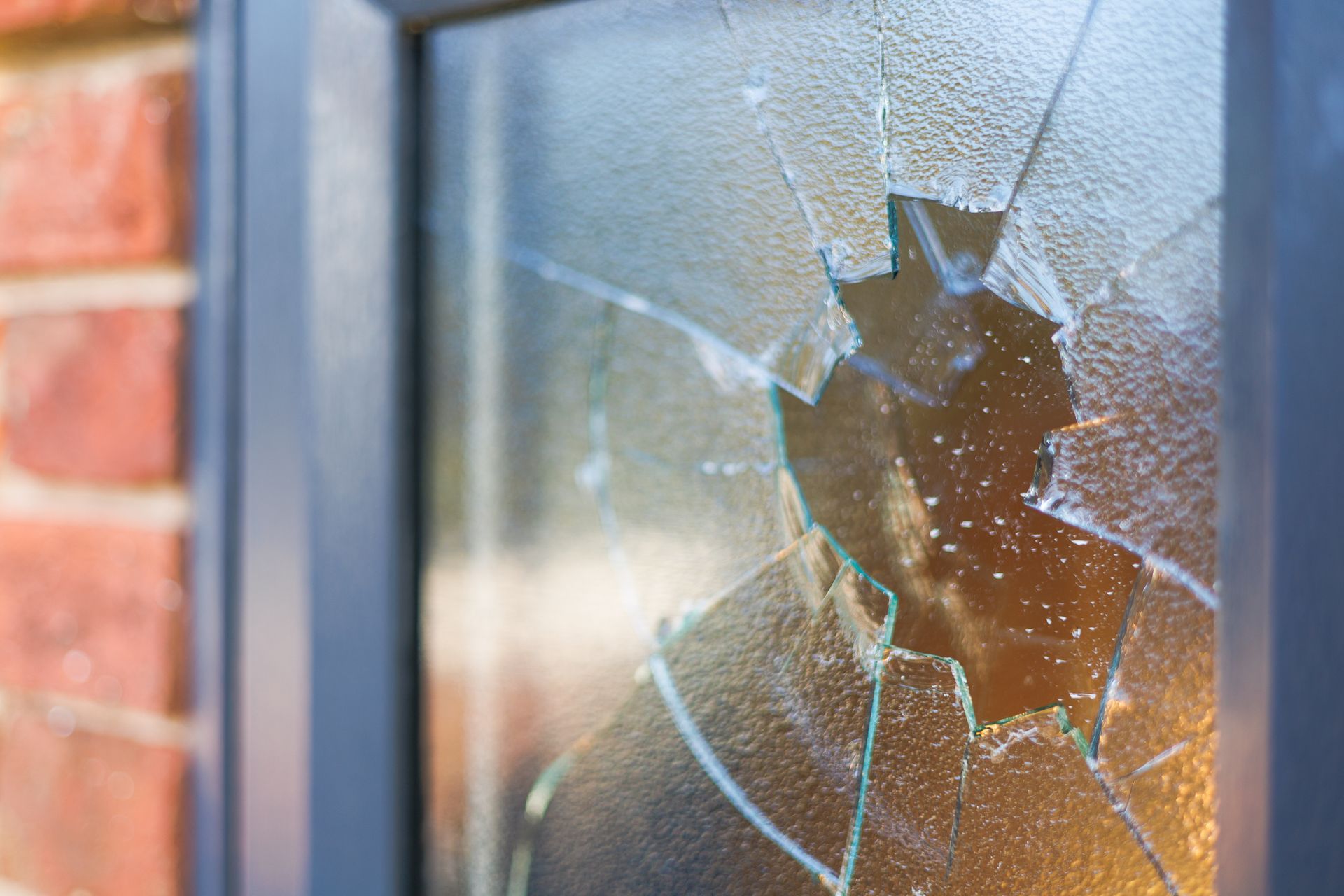 Shattered glass window with a blurred silhouette behind it and a brick wall on the left
