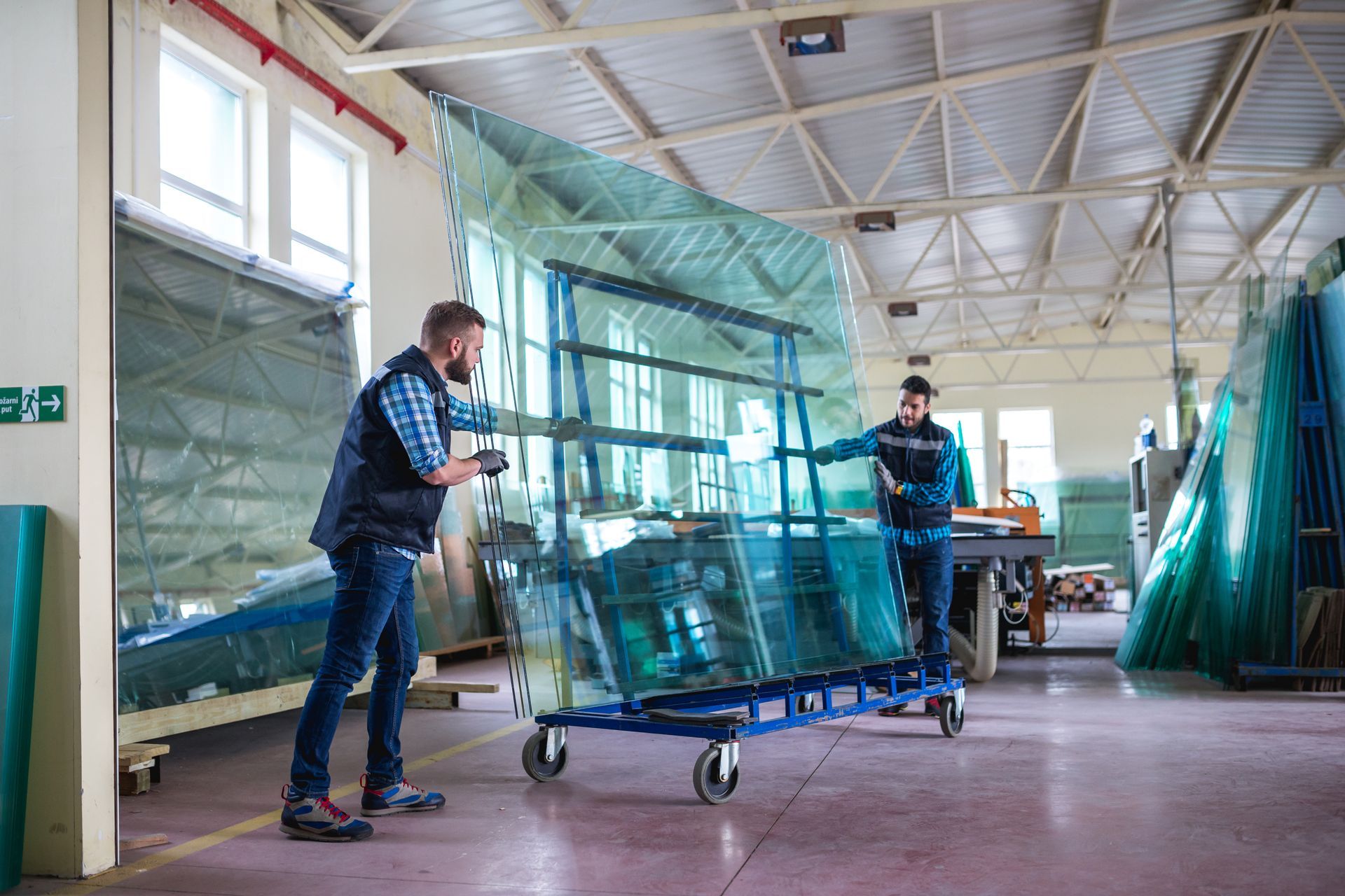 Workers moving a large blue glass panel on a cart in a workshop or warehouse