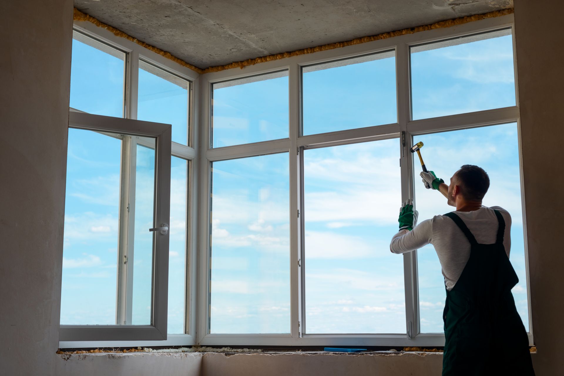 Person cleaning tall windows with a squeegee in a bright room overlooking the sky