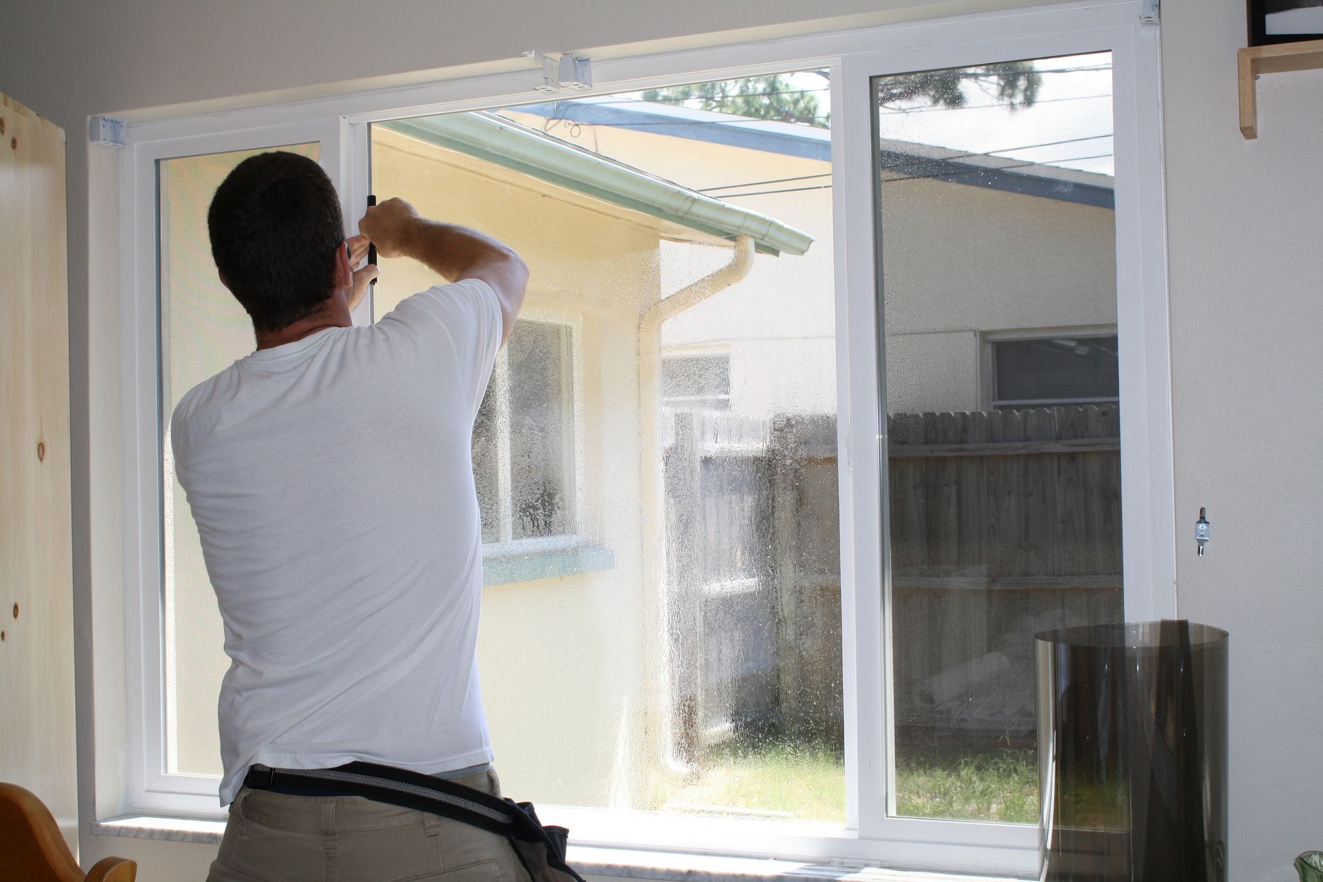 Person cleaning a large window with a squeegee inside a home