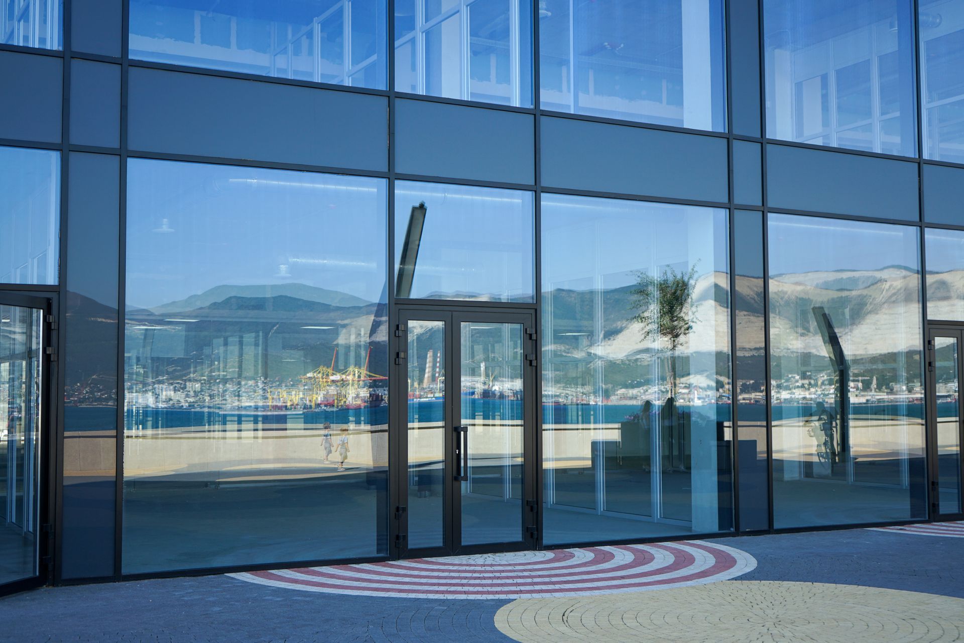 Glass building entrance reflecting mountains and water, with a circular pattern on the ground