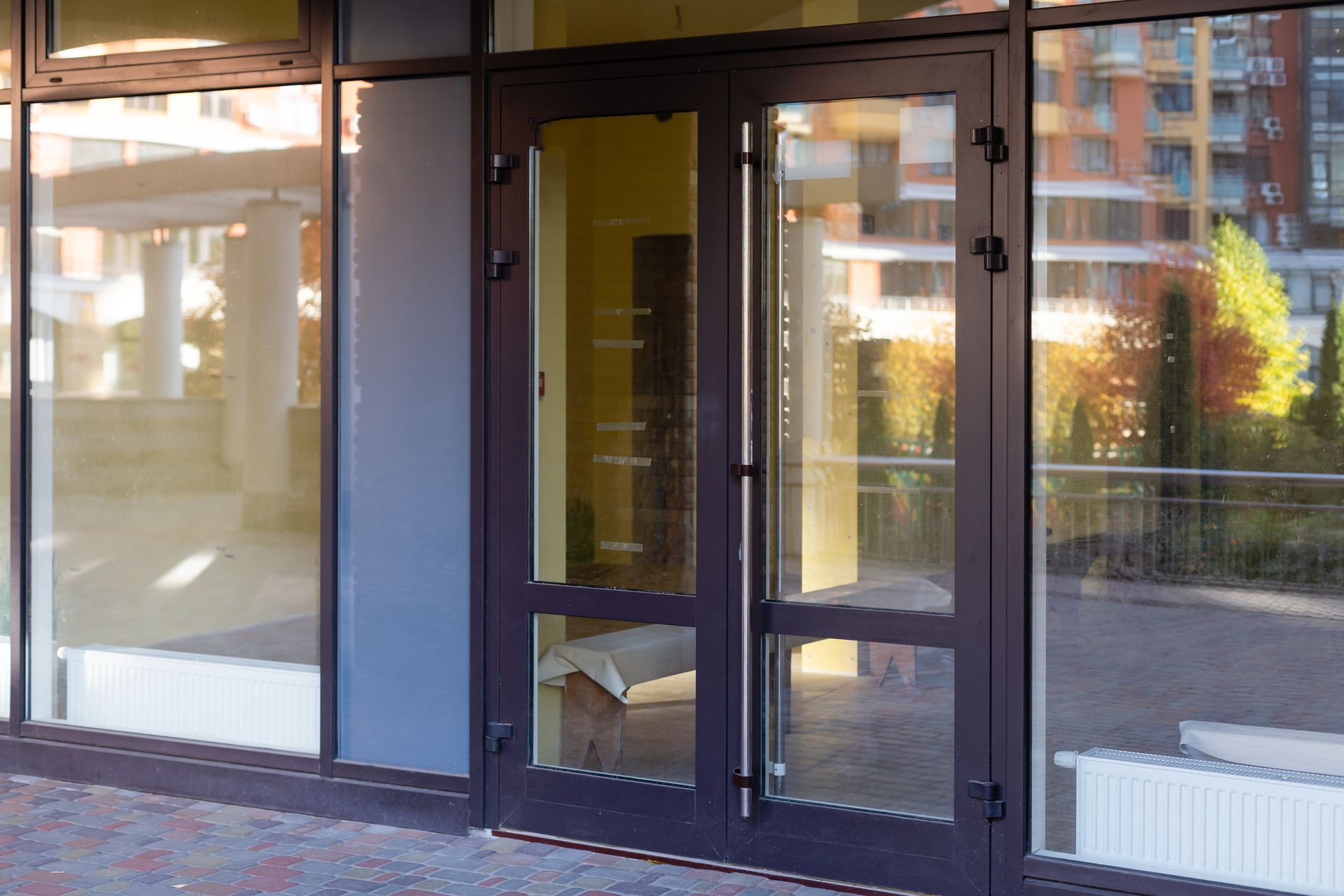 Storefront entrance with glass door and windows, reflecting nearby buildings.