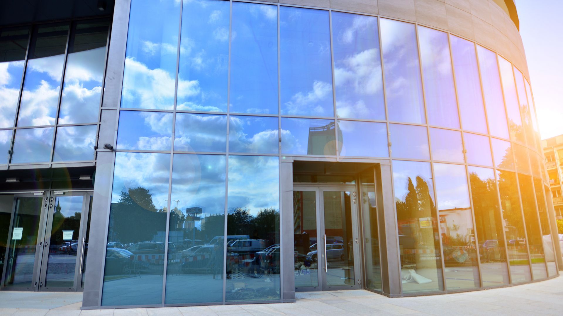 Modern glass building exterior with curved facade reflecting blue sky and sun glare