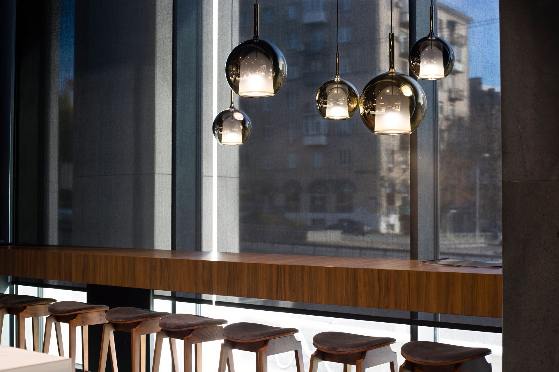 Modern café interior with hanging pendant lights, wooden stools, and large city-view windows.