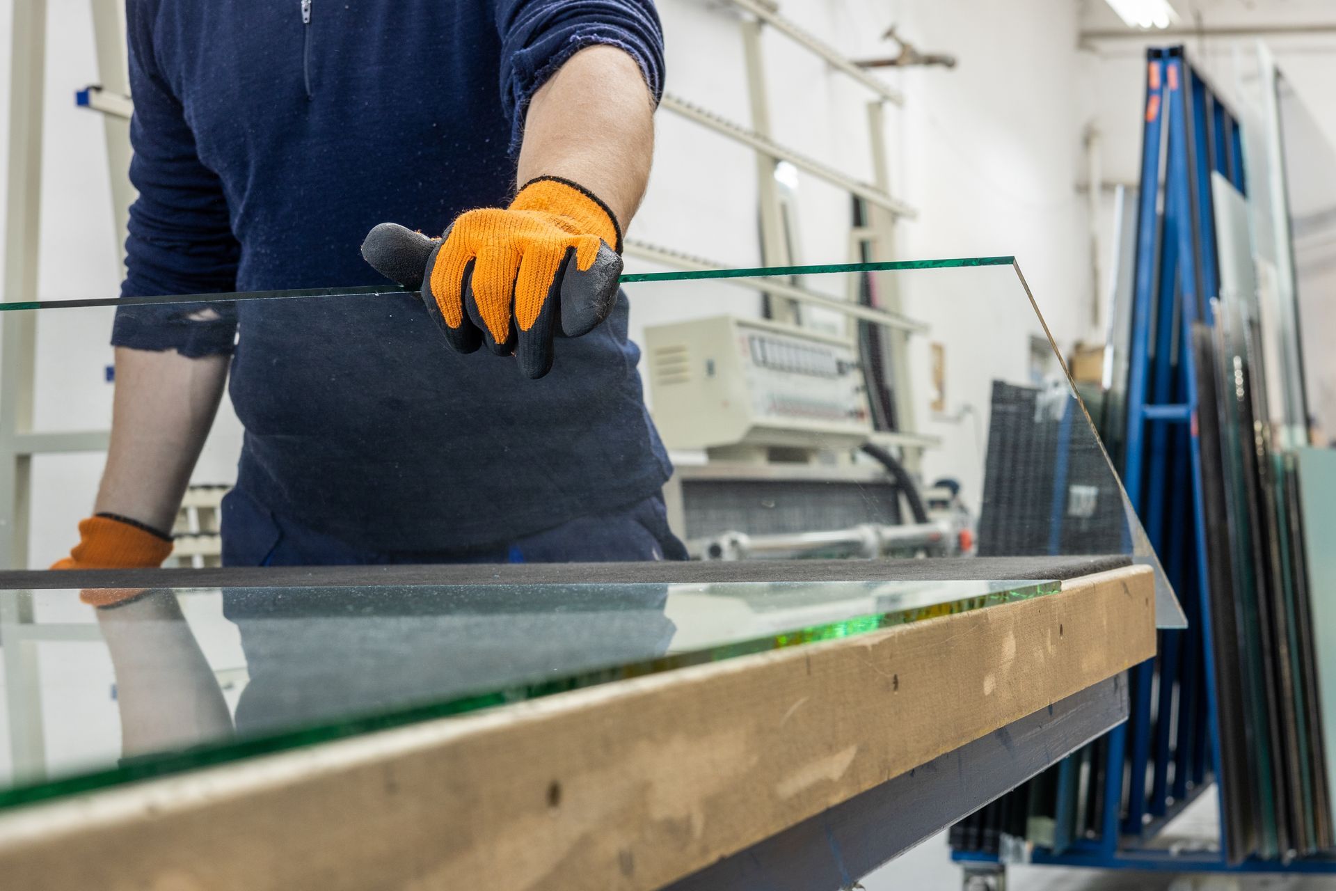 Person in orange gloves handling a glass pane in a workshop