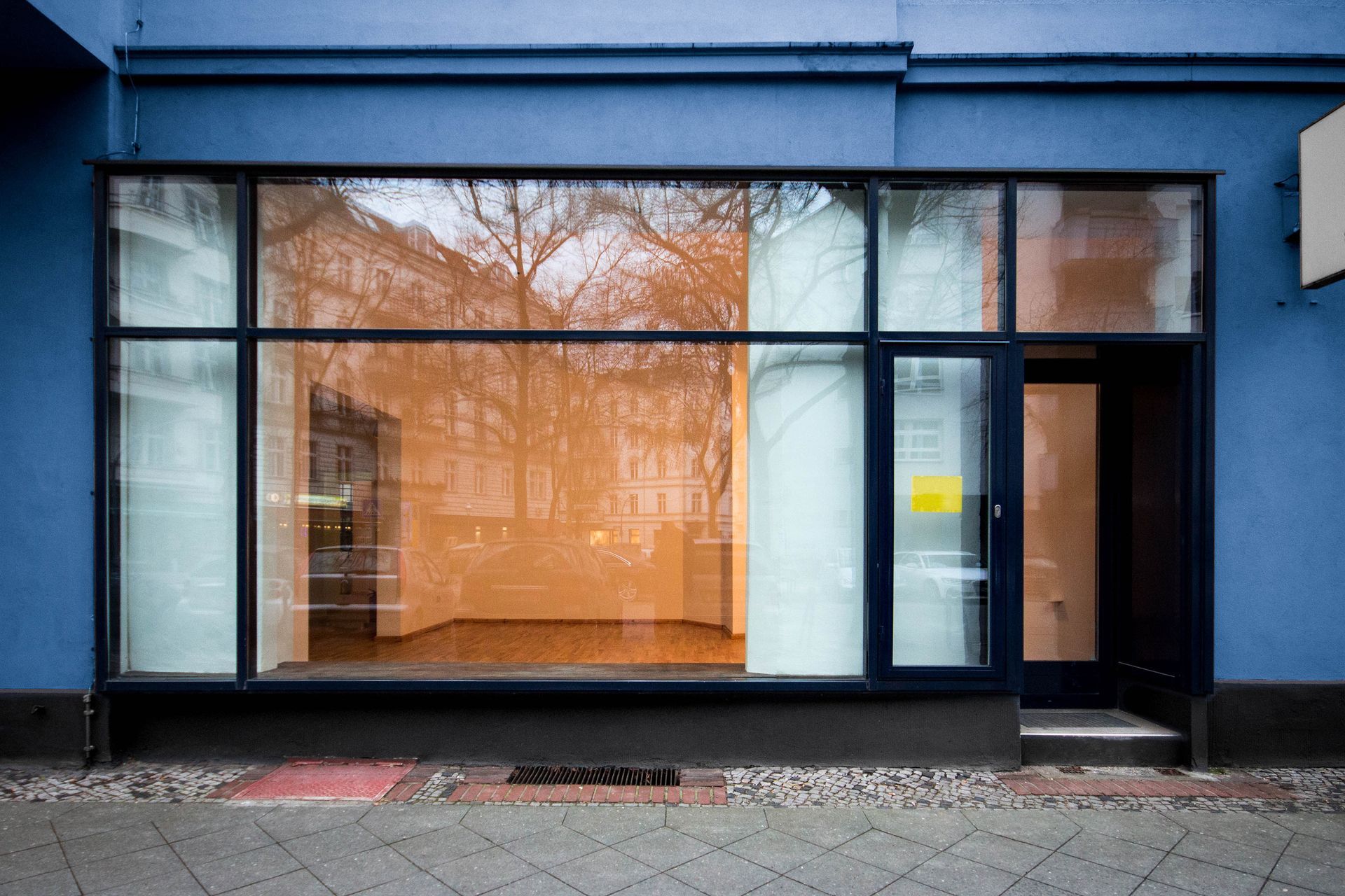 Blue storefront with large orange-tinted display window and black-framed glass door
