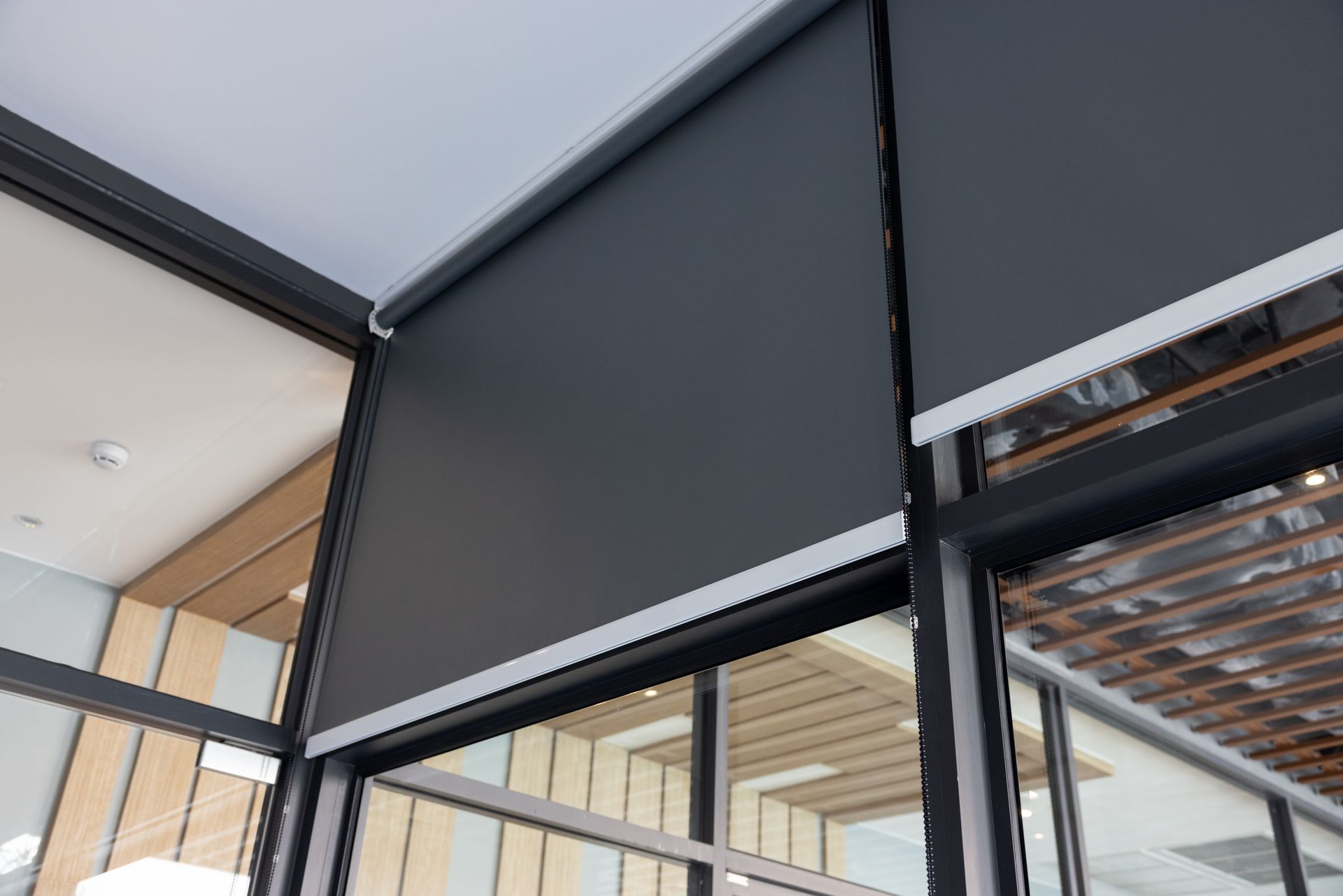 Black roller shade covering a large window in a modern indoor-outdoor space