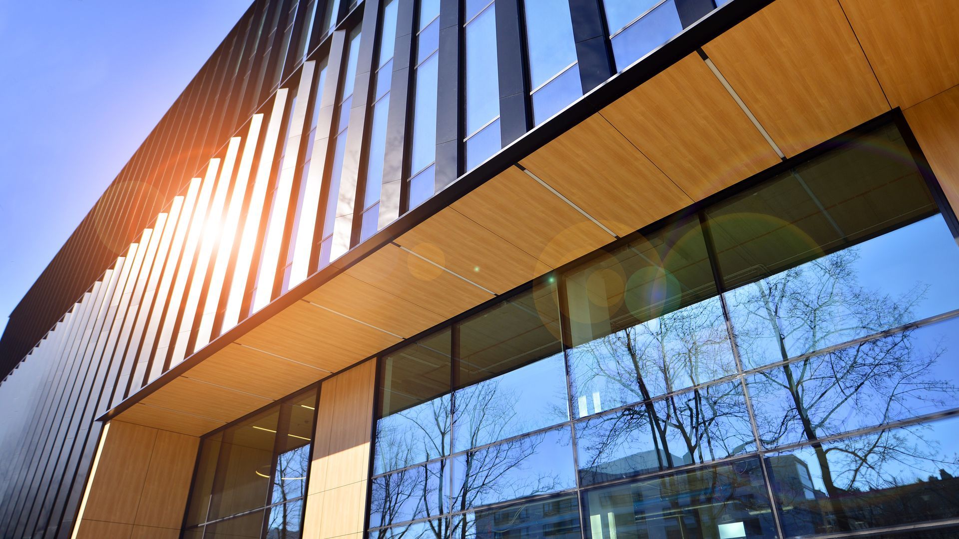 Modern building exterior with wood paneling and reflective glass windows in sunlight