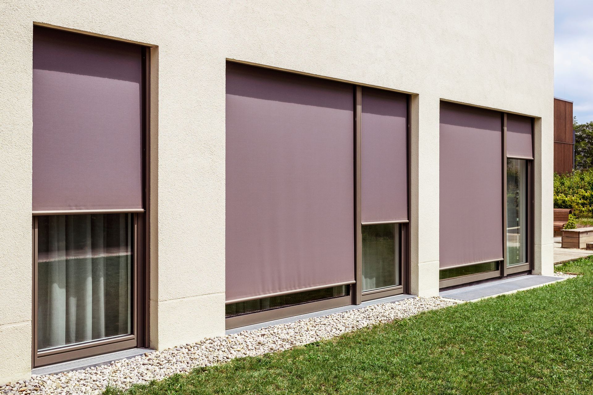House exterior with three windows covered by closed purple roller blinds and a green lawn