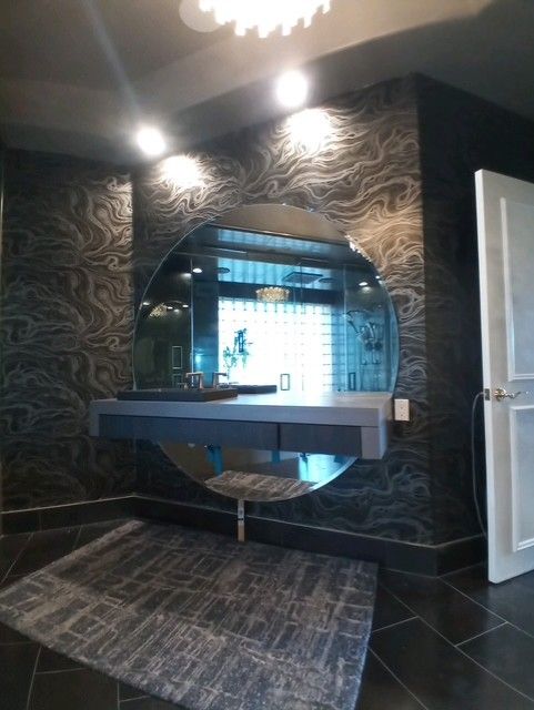 Modern bathroom with patterned wallpaper, wall-mounted sink, round mirror, and tiled floor