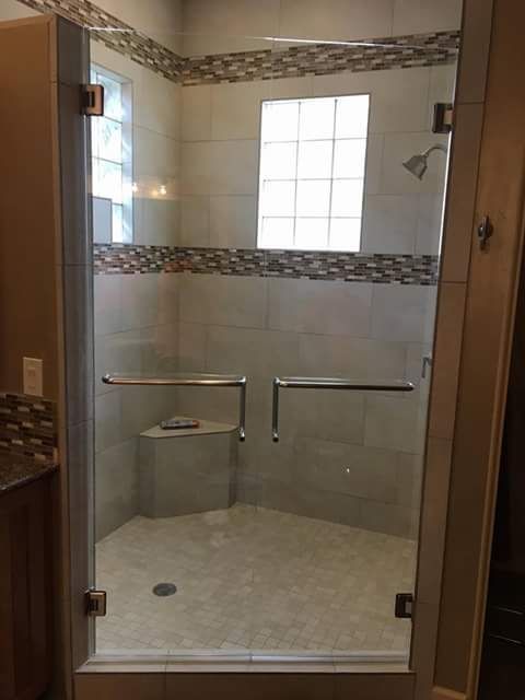 Empty walk-in shower with glass door, beige tile, and decorative mosaic border.