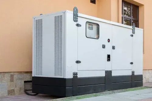 Large white generator next to a light-colored building; black base and vents, small window.