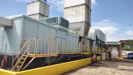 Industrial machinery, light blue exterior with yellow railing, against a blue sky.