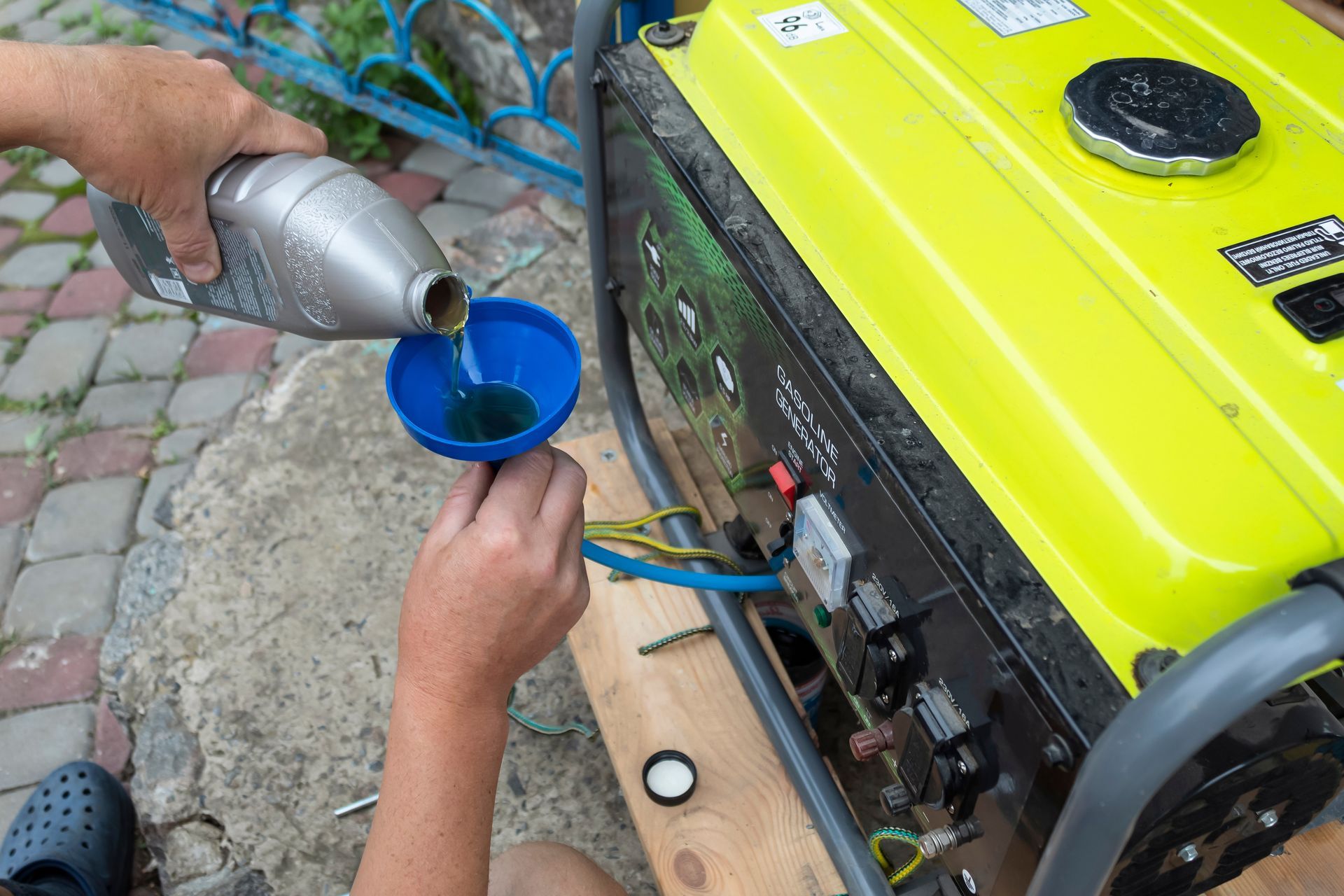 Person pouring oil into a generator using a funnel. The generator is lime green and outdoors.