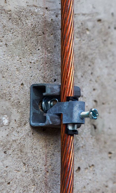 Copper grounding wire secured to concrete wall with a metallic clamp.