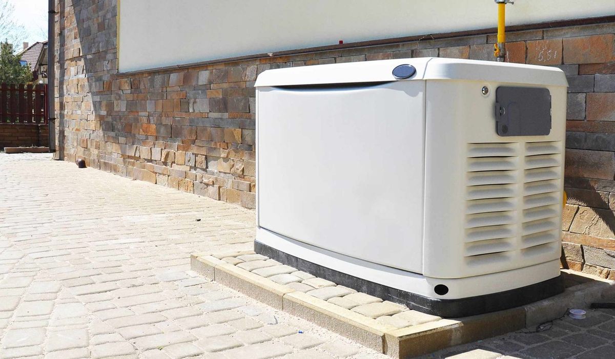 White generator on a brick base beside a stone and white wall.