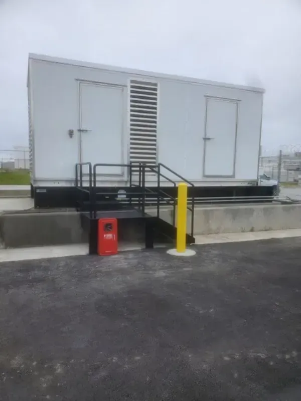 White building with black stairs, yellow bollard, and red fire extinguisher. Outdoors.