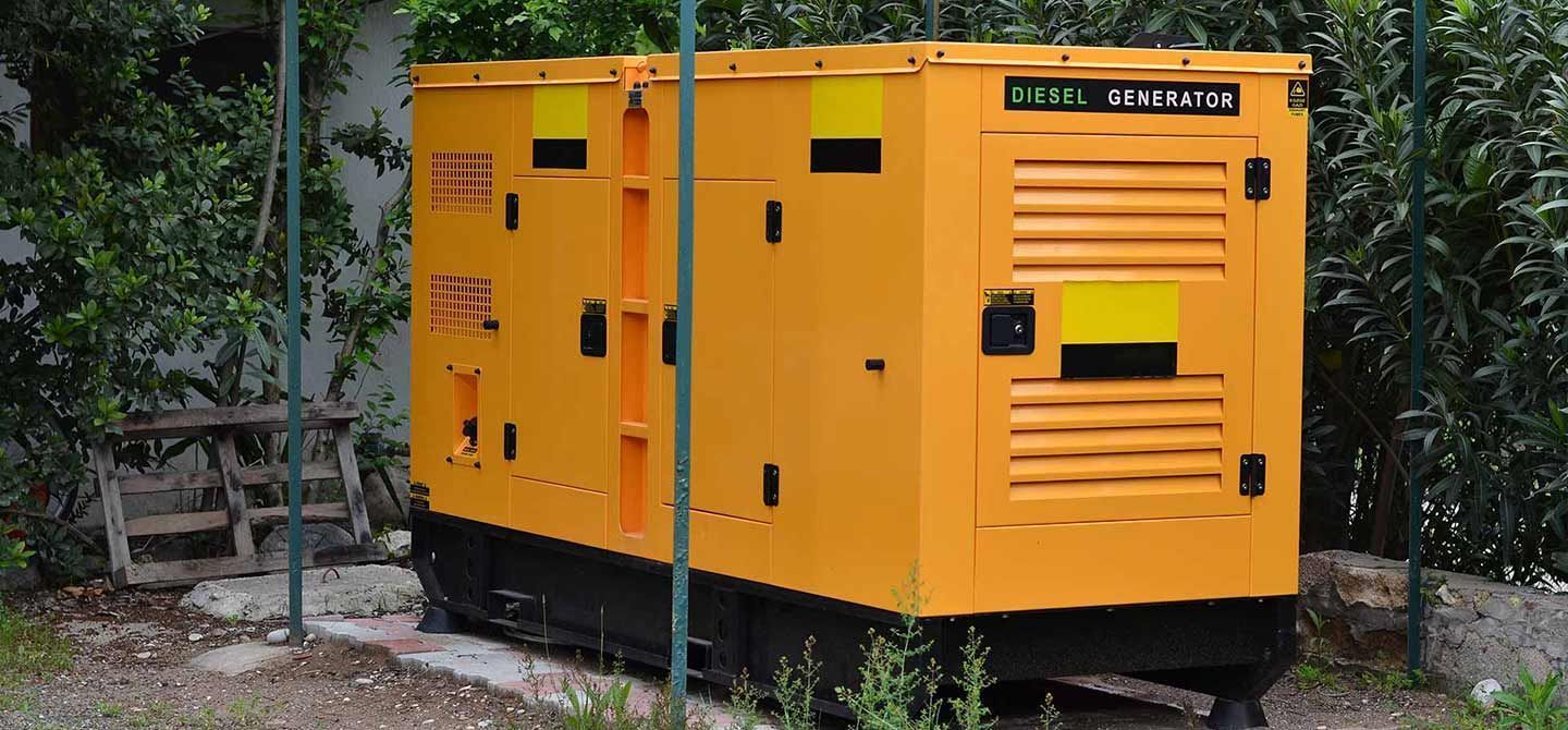 Yellow industrial generator outside, near greenery.