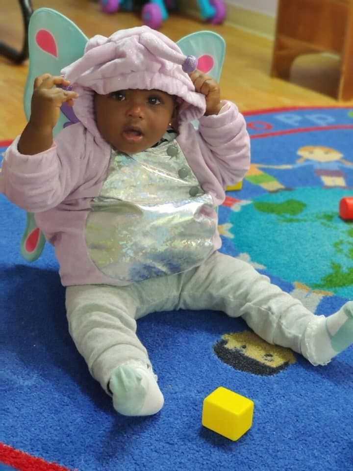 Baby in a hooded outfit sitting on a play mat